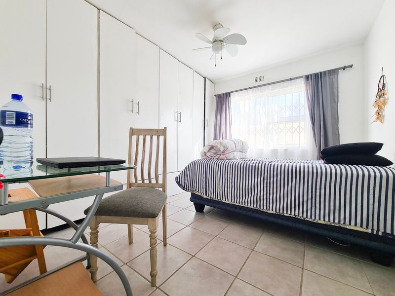A functional bedroom featuring extensive built-in cupboards, tiled flooring, and a ceiling fan, providing ample storage and comfortable living space.