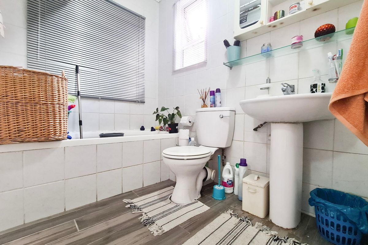 A functional bathroom featuring a pedestal basin, built-in bathtub, and wall-mounted storage, finished with ceramic tiling and neutral flooring.