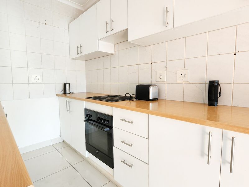 A functional kitchen featuring white cabinetry, laminate countertops, a built-in oven with electric hob, and tiled finishes throughout.