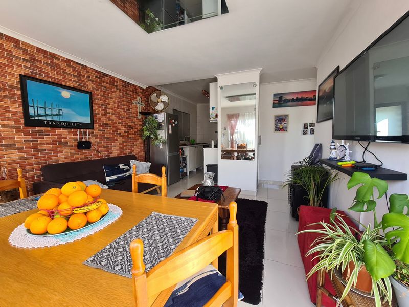 Open-plan living and dining area featuring an exposed brick wall, tiled flooring, and a functional kitchen layout with integrated cabinetry.