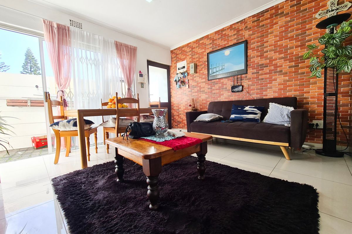 A living room featuring an exposed brick accent wall, tiled flooring, and a sliding glass door providing access to an outdoor area.