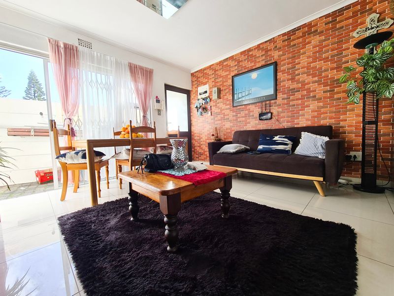 A living room featuring an exposed brick accent wall, tiled flooring, and a sliding glass door providing access to an outdoor area.