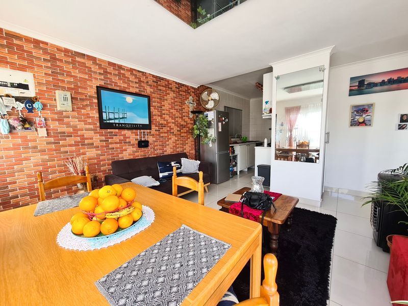Open-plan living and dining area featuring an exposed brick wall, tiled flooring, and an integrated kitchen space with built-in cabinetry.