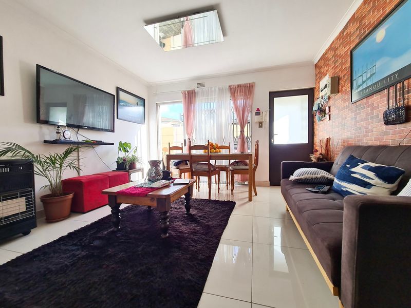 Open-plan living and dining area featuring tiled flooring, a brick-effect feature wall, and direct access to an outdoor space through a sliding glass door.