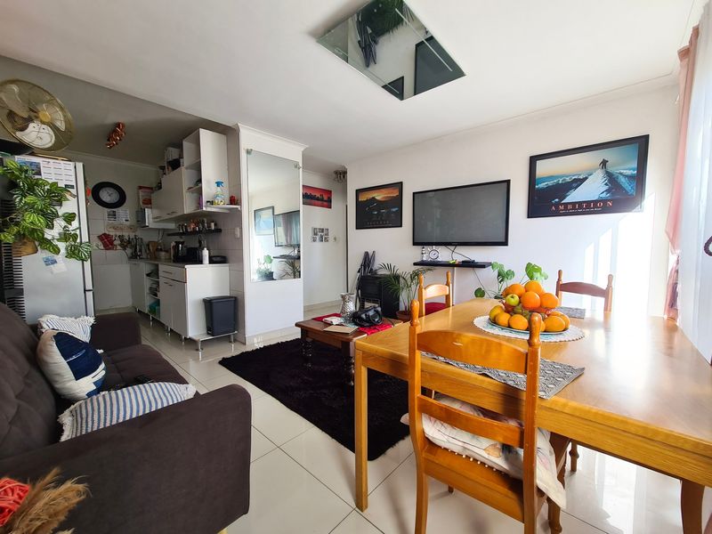 Open-plan living and dining area featuring tiled flooring, integrated kitchen cabinetry, and a mirrored wall accent in a functional apartment layout.
