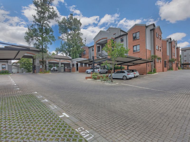 Front exterior view of the apartment complex featuring a paved driveway, covered parking bays, and secure gated access.