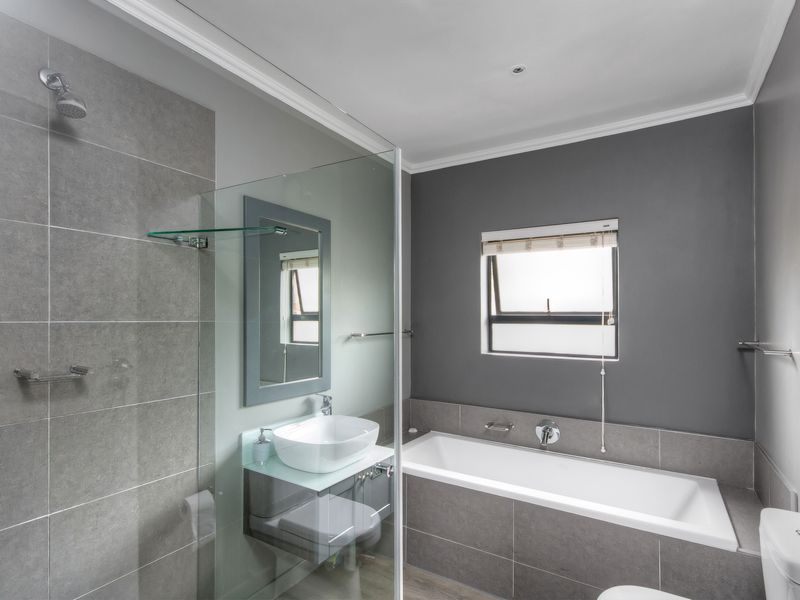 Modern bathroom featuring a glass-enclosed shower, built-in bathtub, vessel sink vanity, and neutral grey tiling.