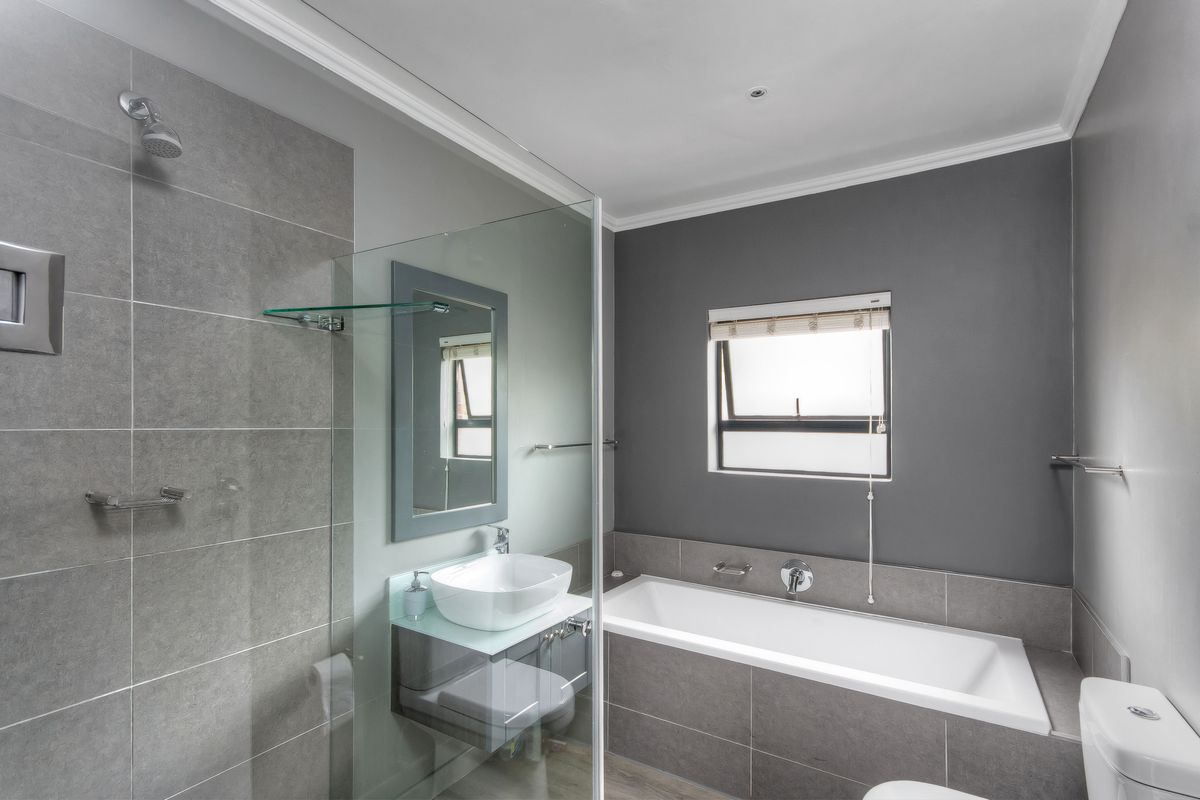 Modern bathroom featuring a glass-enclosed shower, built-in bathtub, vessel sink vanity, and neutral grey tiling.