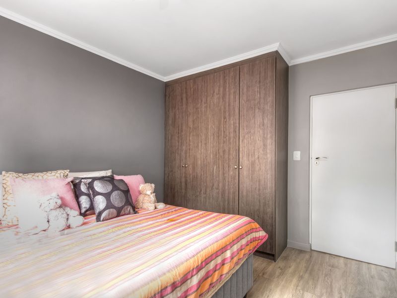 A well-maintained bedroom featuring wood-grain built-in wardrobes, light laminate flooring, and neutral grey wall finishes.