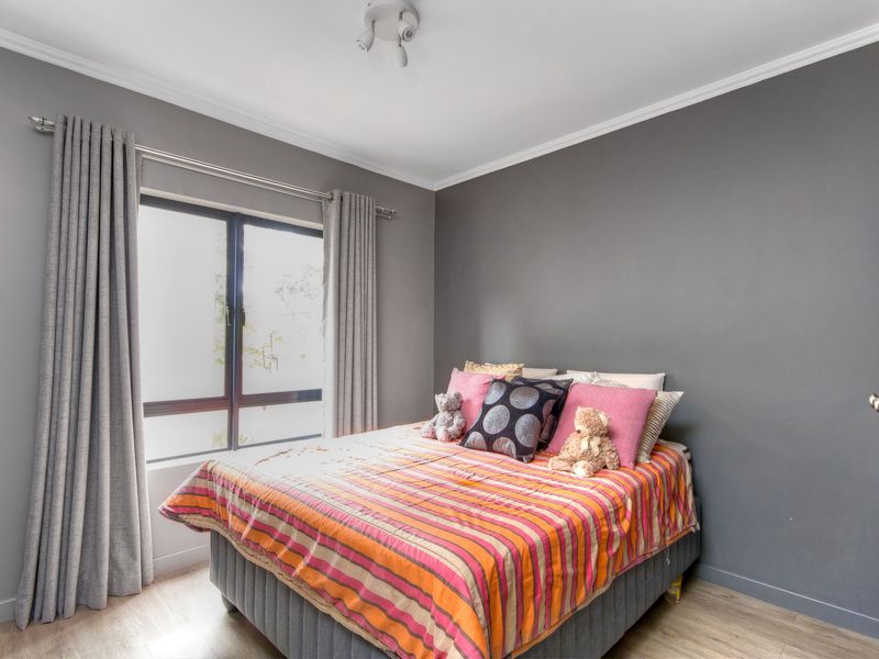 A well-maintained bedroom featuring grey painted walls, crown molding, and light-toned laminate flooring with a window providing natural light.