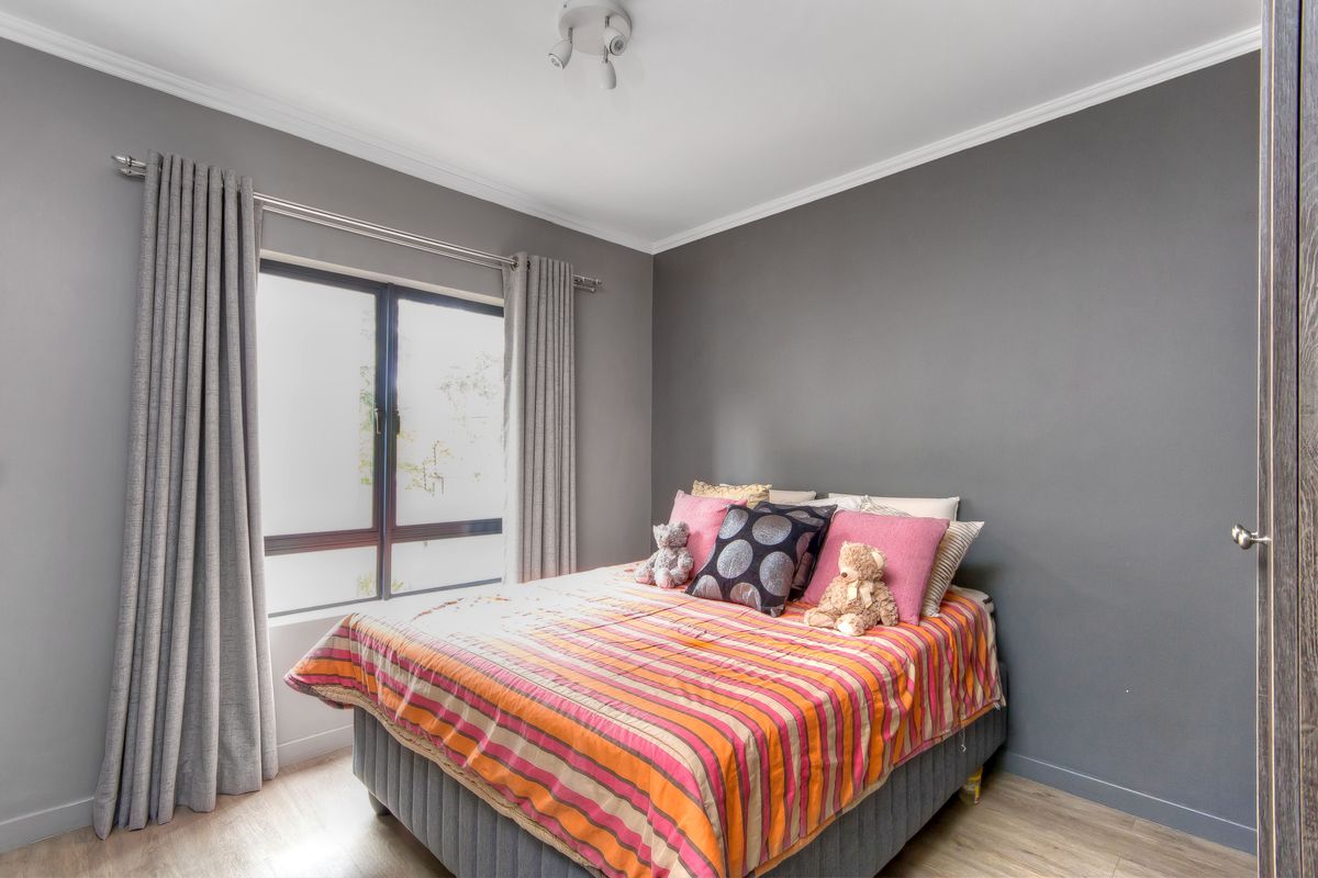 A well-maintained bedroom featuring grey painted walls, crown molding, and light-toned laminate flooring with a window providing natural light.