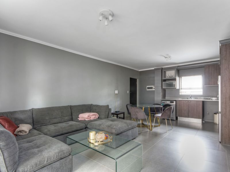 Open plan living area featuring a modern kitchen with built-in cabinetry, tiled flooring, and integrated appliances, seamlessly connected to the lounge space.