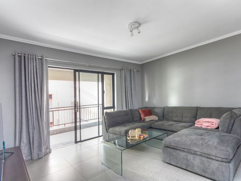 A bright living room featuring neutral tiled flooring, grey walls, and a sliding glass door providing access to an outdoor balcony area.