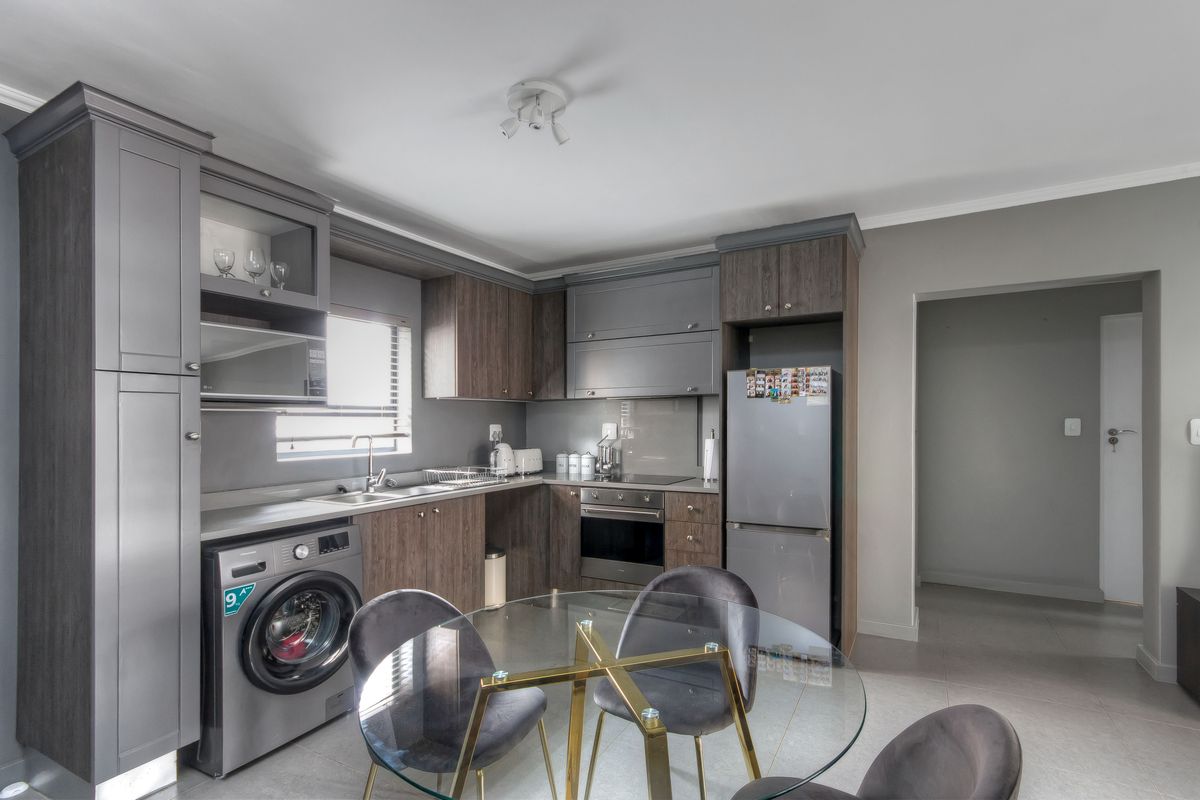 Modern kitchen featuring dark wood-toned cabinetry, integrated appliances, stainless steel sink, and tiled flooring, offering a functional and contemporary cooking space.