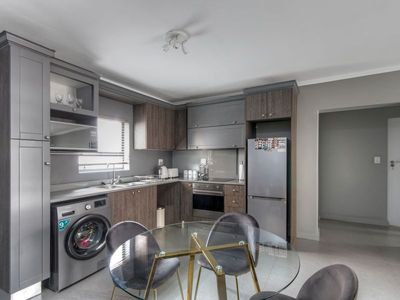 Modern kitchen featuring dark wood-toned cabinetry, integrated appliances, stainless steel sink, and tiled flooring, offering a functional and contemporary cooking space.