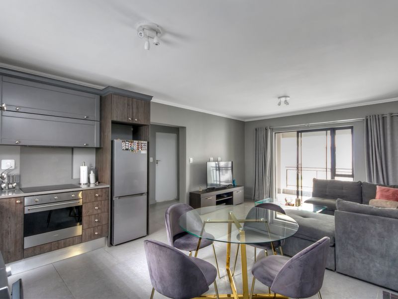 Modern open-plan living area featuring a contemporary kitchen with built-in cabinetry, electric oven, hob, and seamless flow to the living space and balcony.