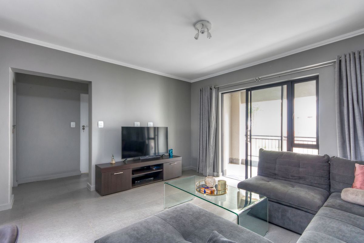 A well-maintained living room featuring neutral grey walls, tiled flooring, and a sliding glass door providing access to an outdoor balcony area.