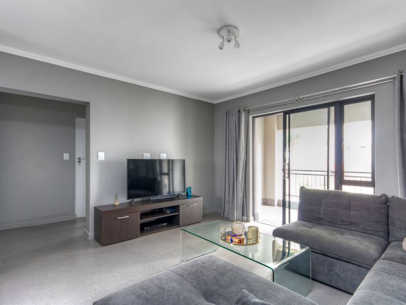 A well-maintained living room featuring neutral grey walls, tiled flooring, and a sliding glass door providing access to an outdoor balcony area.
