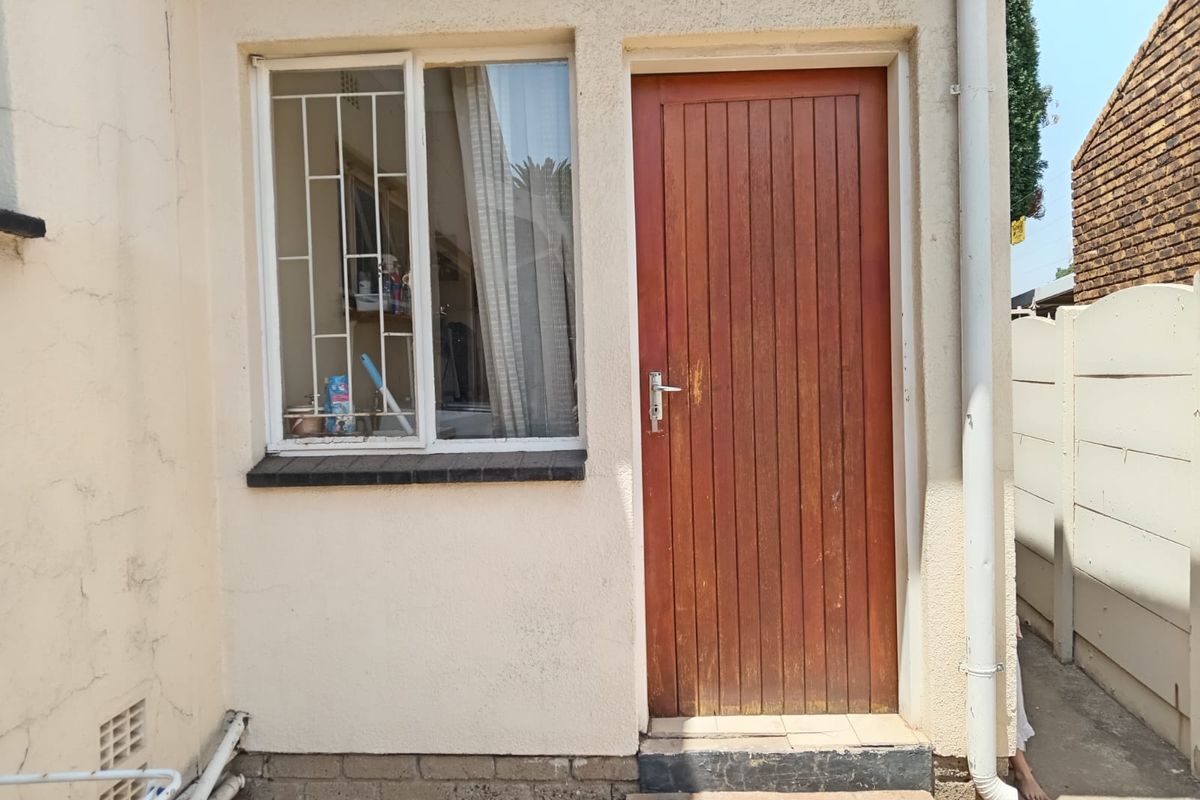 Exterior view of a side entrance featuring a timber door and a window with security bars, showing signs of wear on the facade.