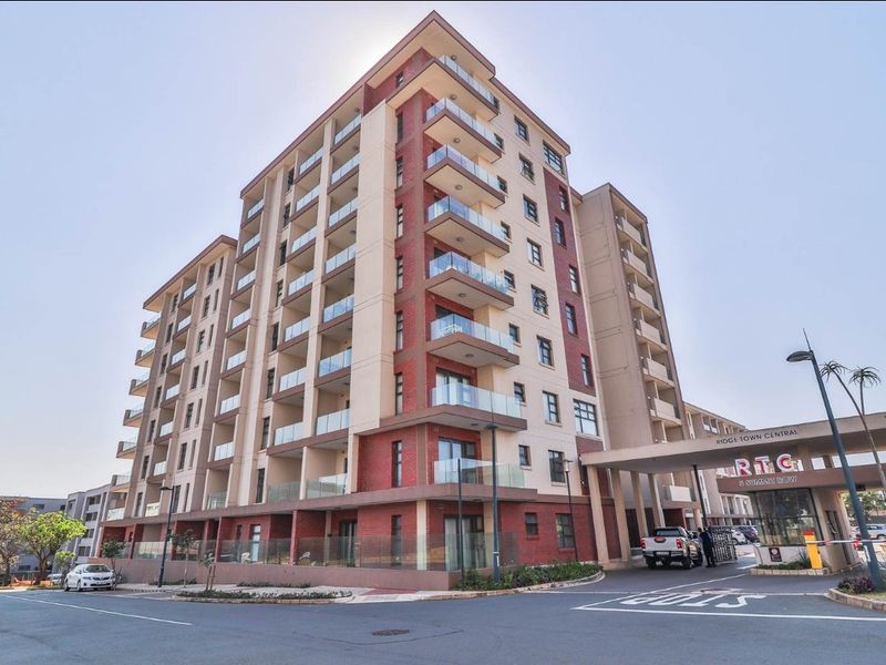 Exterior view of the Ridge Town Central apartment complex, featuring a modern brick facade, glass balconies, and a secure gated entrance.