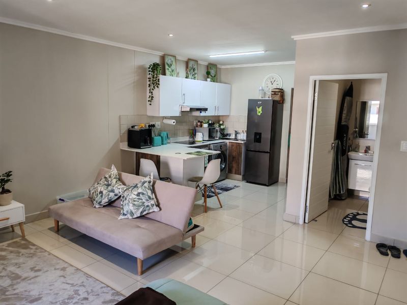 An open-plan living area featuring a compact kitchen with built-in cabinetry, tiled flooring, and recessed lighting, seamlessly connected to the main living space.