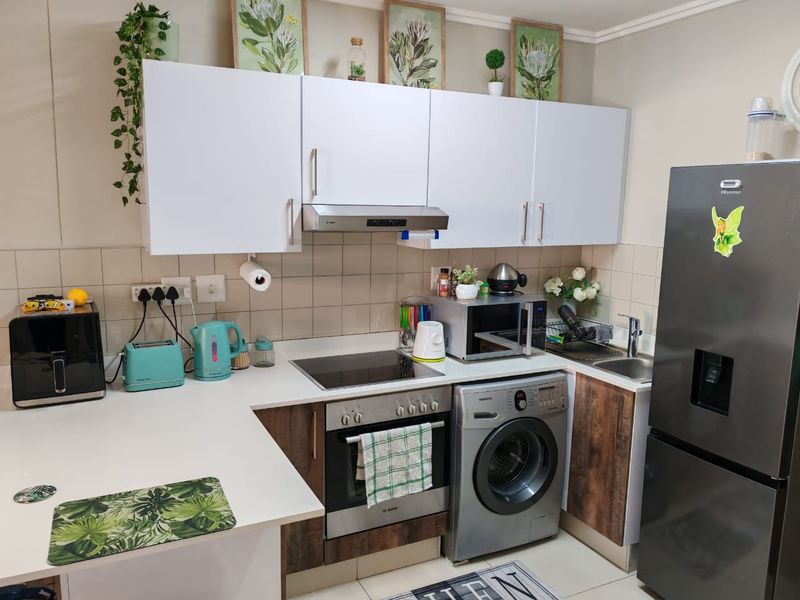 A compact, functional kitchen featuring white upper cabinets, wood-look lower cabinetry, a built-in oven, electric cooktop, and an integrated washing machine.