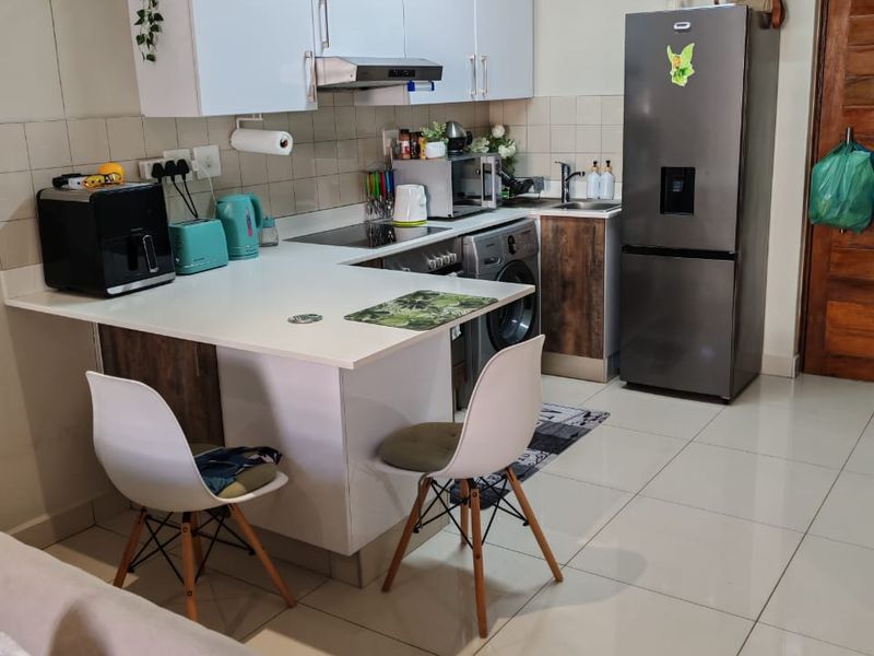 Open-plan kitchen featuring white cabinetry, a breakfast counter, integrated appliances, and tiled flooring, seamlessly connecting to the living area.