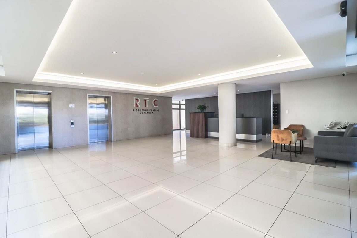 Modern apartment building lobby featuring polished tiled floors, recessed cove lighting, and dual stainless steel elevators.
