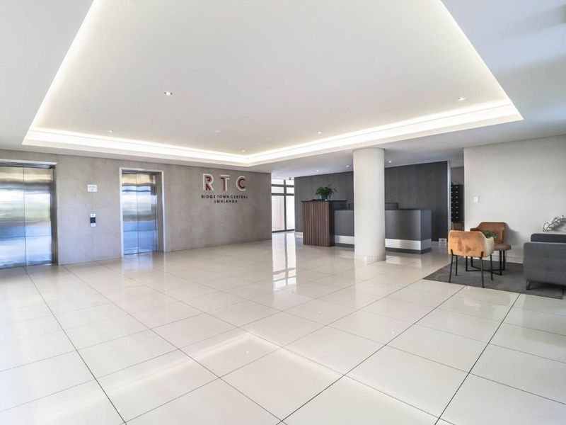 Modern apartment building lobby featuring polished tiled floors, recessed cove lighting, and dual stainless steel elevators.