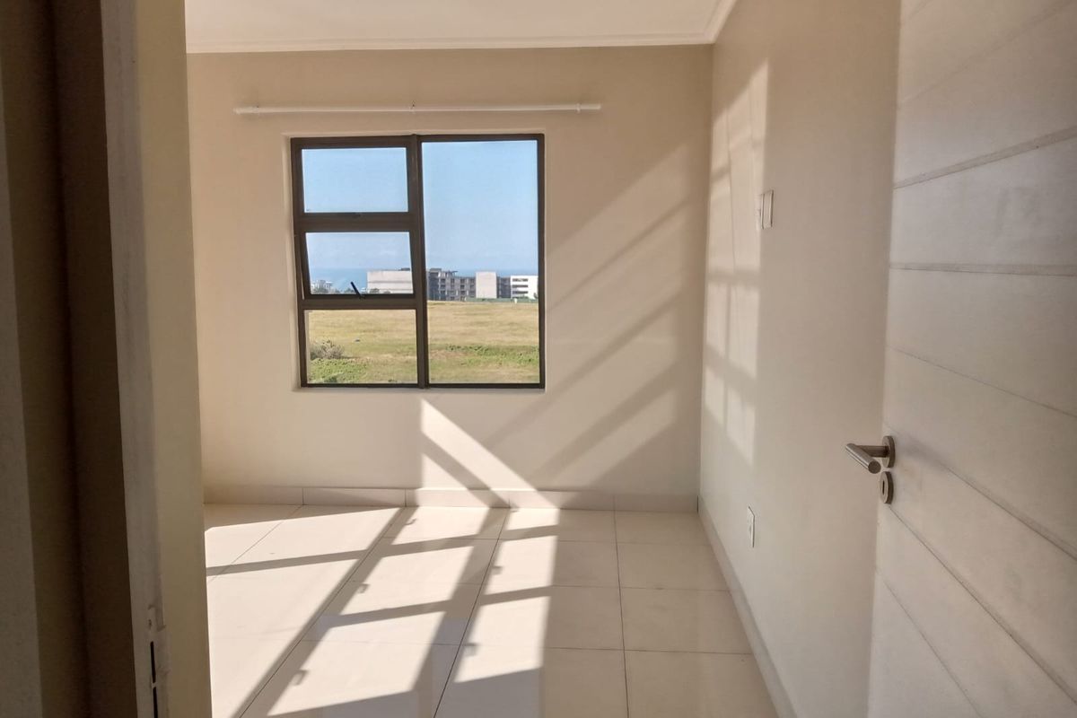 A bright, empty bedroom featuring neutral tiled flooring, clean walls, and a window with a view of the surrounding landscape.