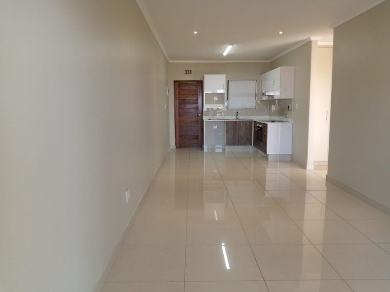 An open-plan living and kitchen area featuring polished tile flooring, modern cabinetry, and integrated kitchen appliances in a clean, vacant space.