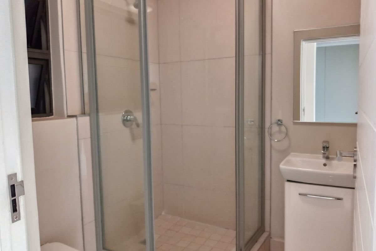 A clean, functional bathroom featuring a glass-enclosed shower, a wall-mounted basin with a vanity cabinet, and a mirror.