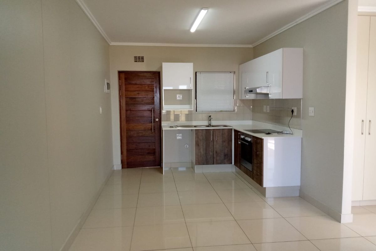 A clean, modern kitchen featuring white and wood-tone cabinetry, integrated appliances, tiled flooring, and a functional layout.
