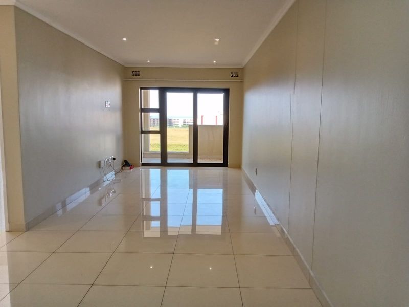 A bright, empty living room featuring polished tiled flooring, recessed downlighting, and a large sliding glass door leading to an outdoor area.