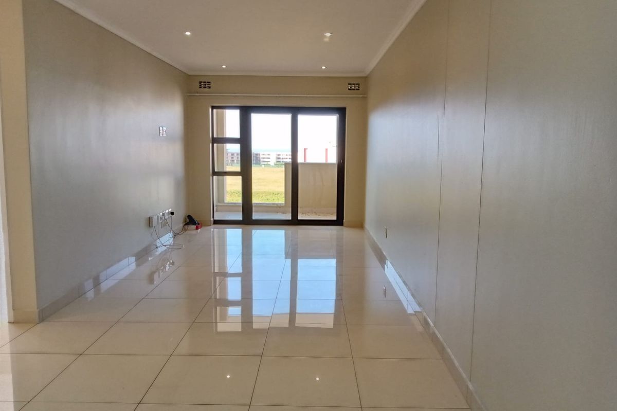 A bright, empty living room featuring polished tiled flooring, recessed downlighting, and a large sliding glass door leading to an outdoor area.