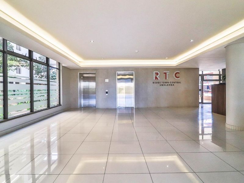 Modern apartment building lobby featuring tiled floors, recessed lighting, and dual elevator access with a professional reception area.