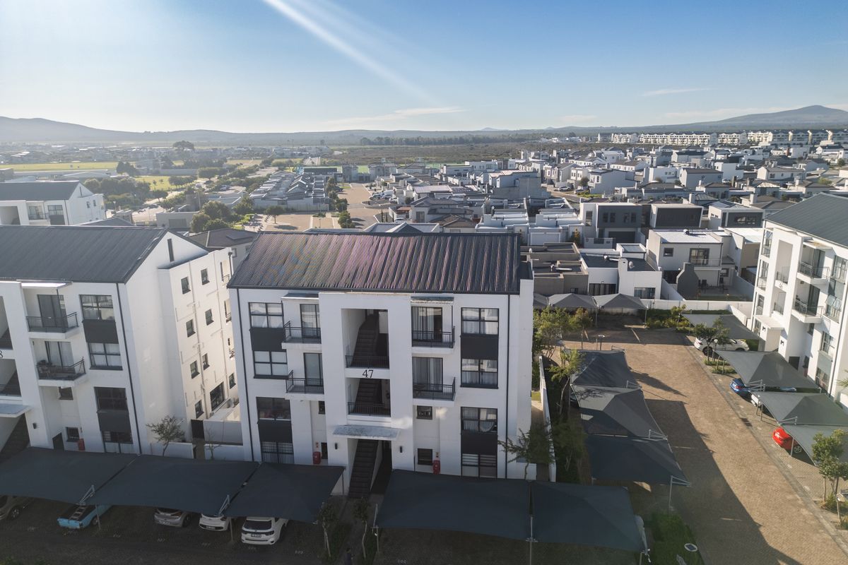 Aerial view of a modern apartment complex featuring white facades, dark metal roofing, and dedicated covered parking areas within a residential estate.