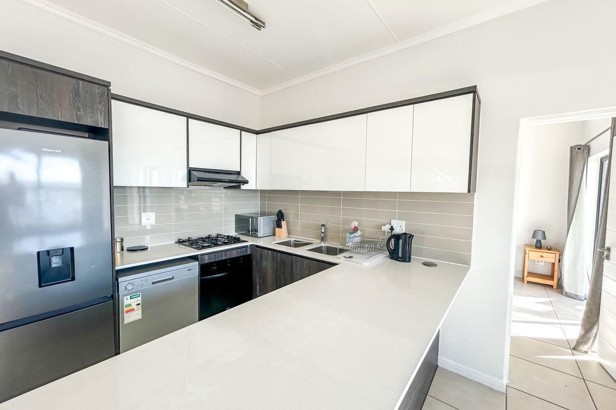 Modern kitchen featuring sleek white and dark cabinetry, stone countertops, gas hob, extractor fan, and integrated stainless steel sink with tiled backsplash.