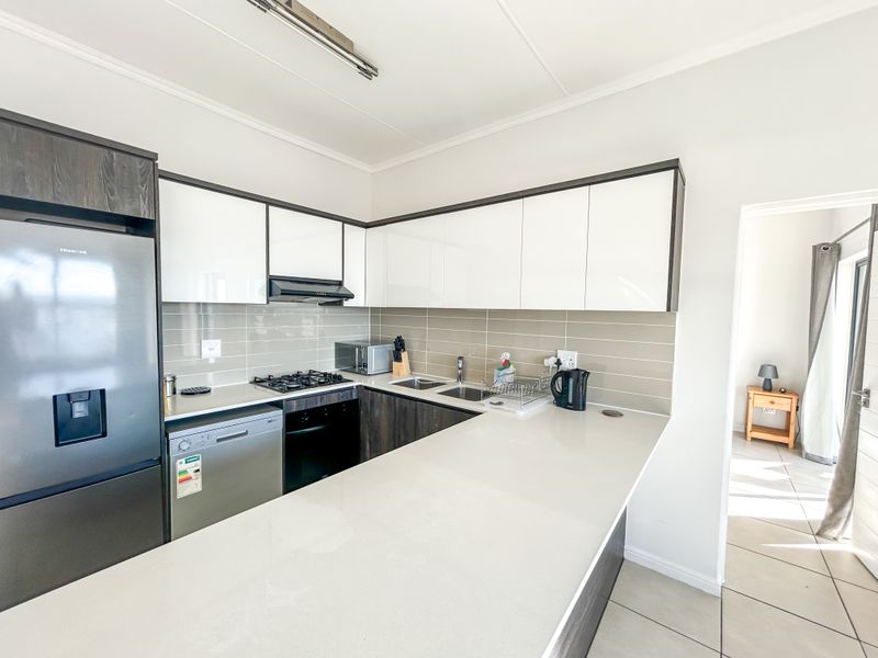 Modern kitchen featuring sleek white and dark cabinetry, stone countertops, gas hob, extractor fan, and integrated stainless steel sink with tiled backsplash.