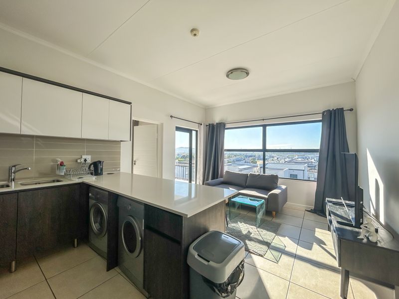 Modern open-plan living area featuring a sleek kitchen with integrated appliances, tiled flooring, and large windows offering expansive views.