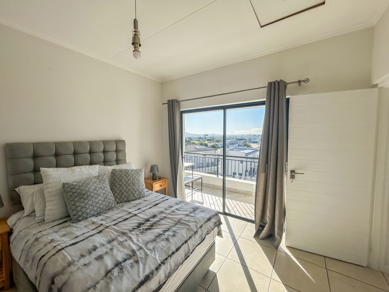 A bright bedroom featuring tiled flooring and a sliding glass door that opens onto a private balcony with scenic views.