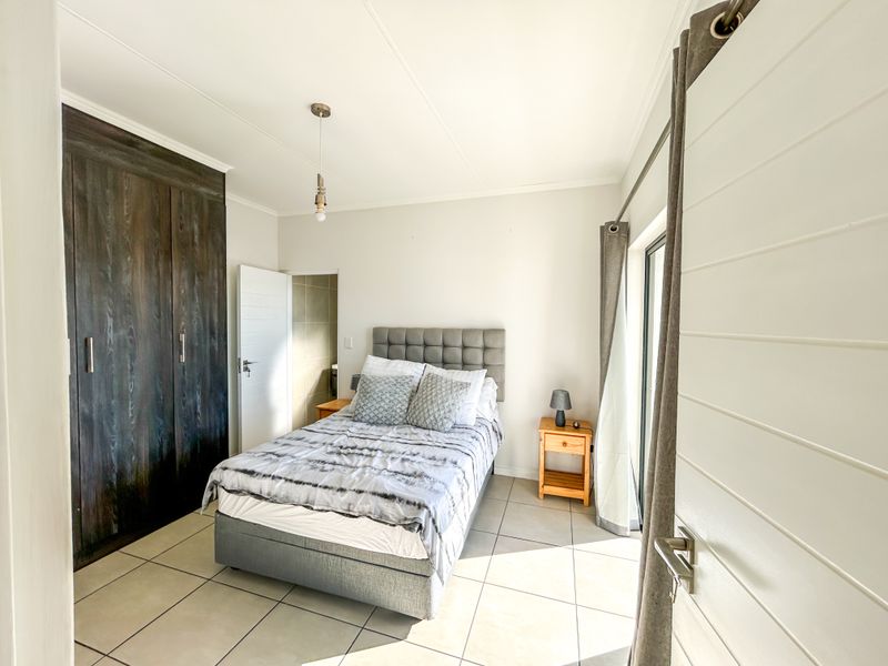 A well-maintained bedroom featuring built-in dark wood cupboards, neutral tiled flooring, and direct access to an outdoor area via a sliding door.