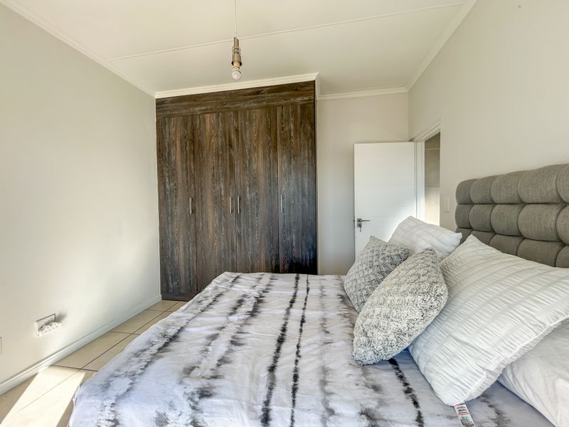 A well-maintained bedroom featuring dark wood-finish built-in cupboards and neutral tiled flooring.