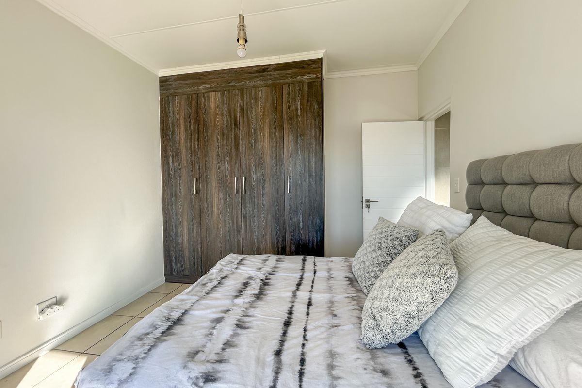 A well-maintained bedroom featuring dark wood-finish built-in cupboards and neutral tiled flooring.
