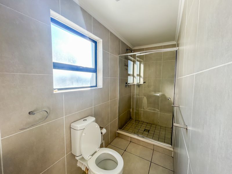 A clean, modern bathroom featuring neutral ceramic wall and floor tiles, a glass-enclosed walk-in shower, and a standard toilet.