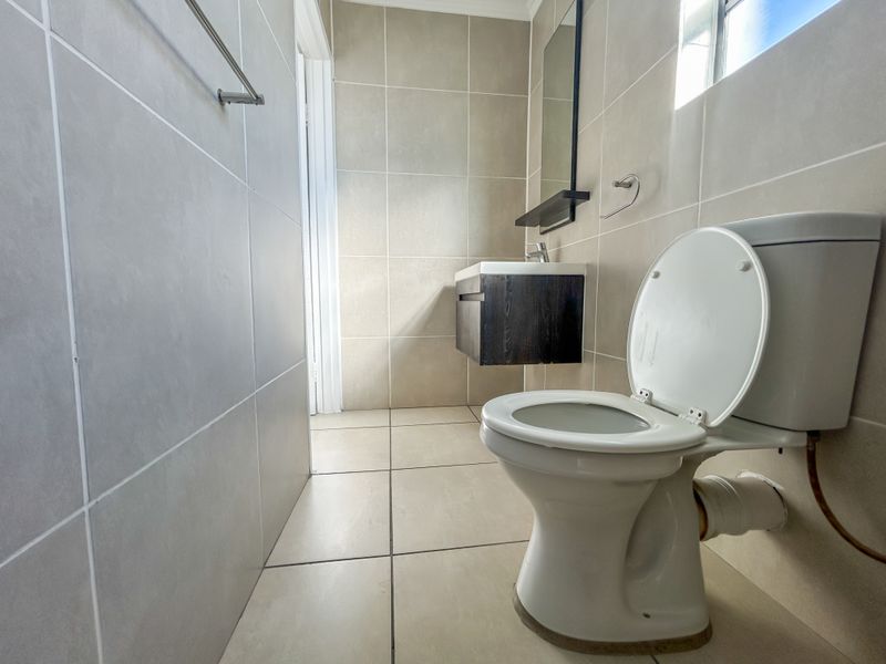 A compact bathroom featuring neutral wall and floor tiling, a wall-mounted vanity, and a standard toilet suite.
