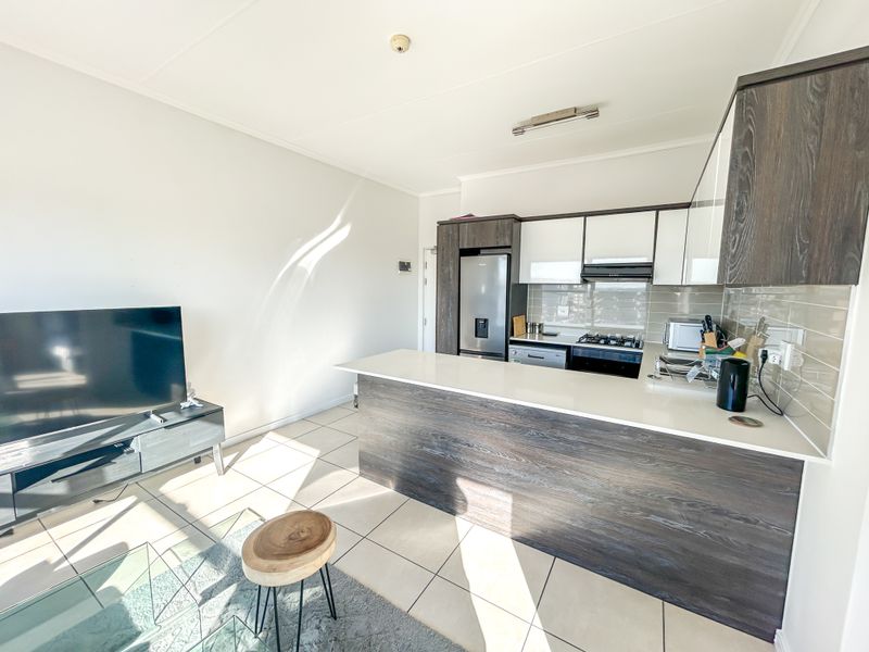Modern open-plan living area featuring a contemporary kitchen with dark wood cabinetry, stone countertops, breakfast bar, and integrated appliances.