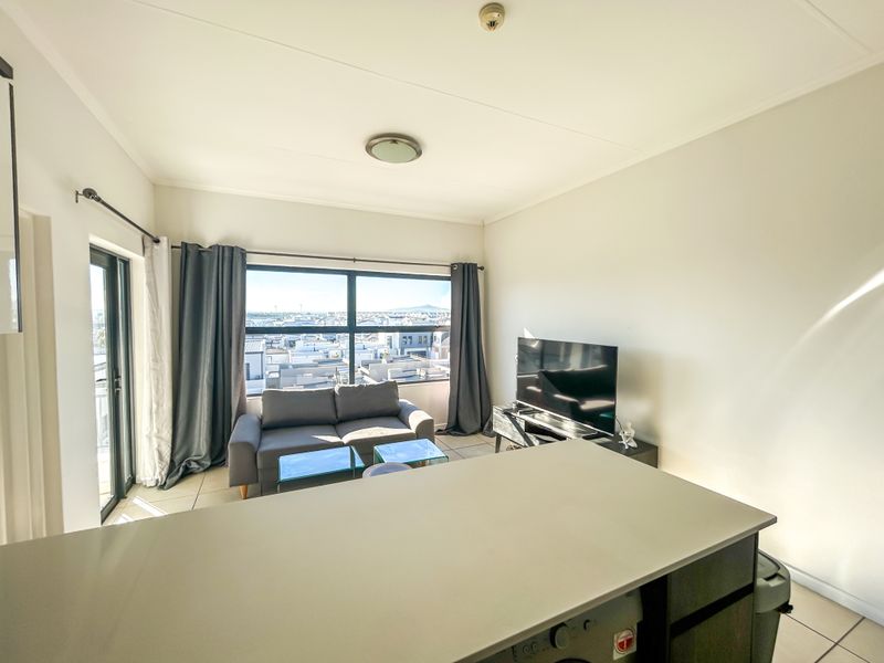 Open plan living area featuring a kitchen island, tiled flooring, and large windows with access to a balcony, offering natural light and urban views.