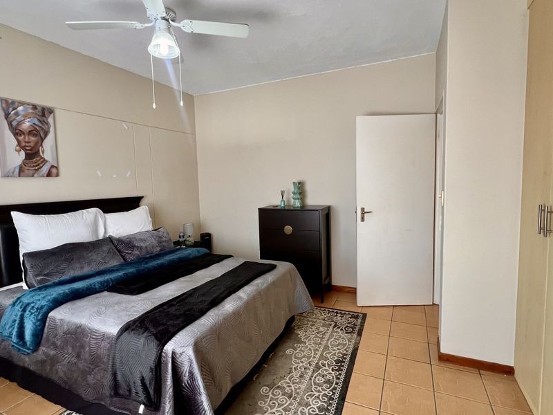 A bedroom featuring tiled flooring, a ceiling fan, and built-in cupboards, providing functional storage and basic amenities.