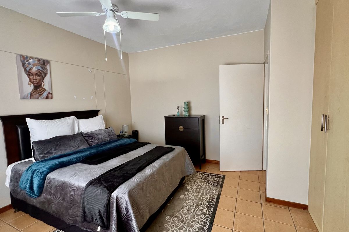 A bedroom featuring tiled flooring, a ceiling fan, and built-in cupboards, providing functional storage and basic amenities.